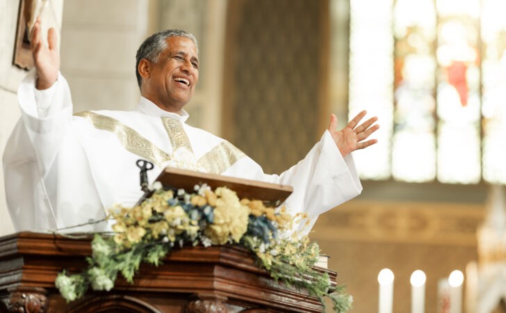 Church leader giving a welcome speech from the pulpit, with the congregation seated and listening during the opening moments of a worship service.